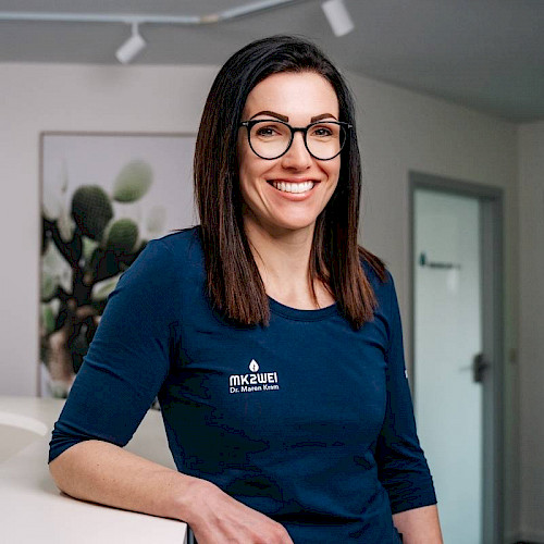 Porträt von Dr. Maren Kram, Zahnarztin in der Praxis MK2WEI in Dettingen an der Iller, lächelnd in blauem Shirt vor Praxisempfang.