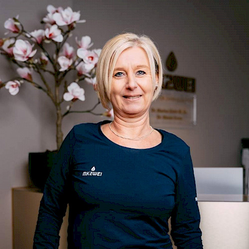 Bild zeigt eine lächelnde Mitarbeiterin von MK2WEi im blauen Obertteil und bloden Haaren.